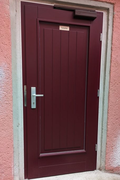 Eine Rotbraun gefärbte Nebeneingangstür aus Holz mit automatischer Schließfunktion